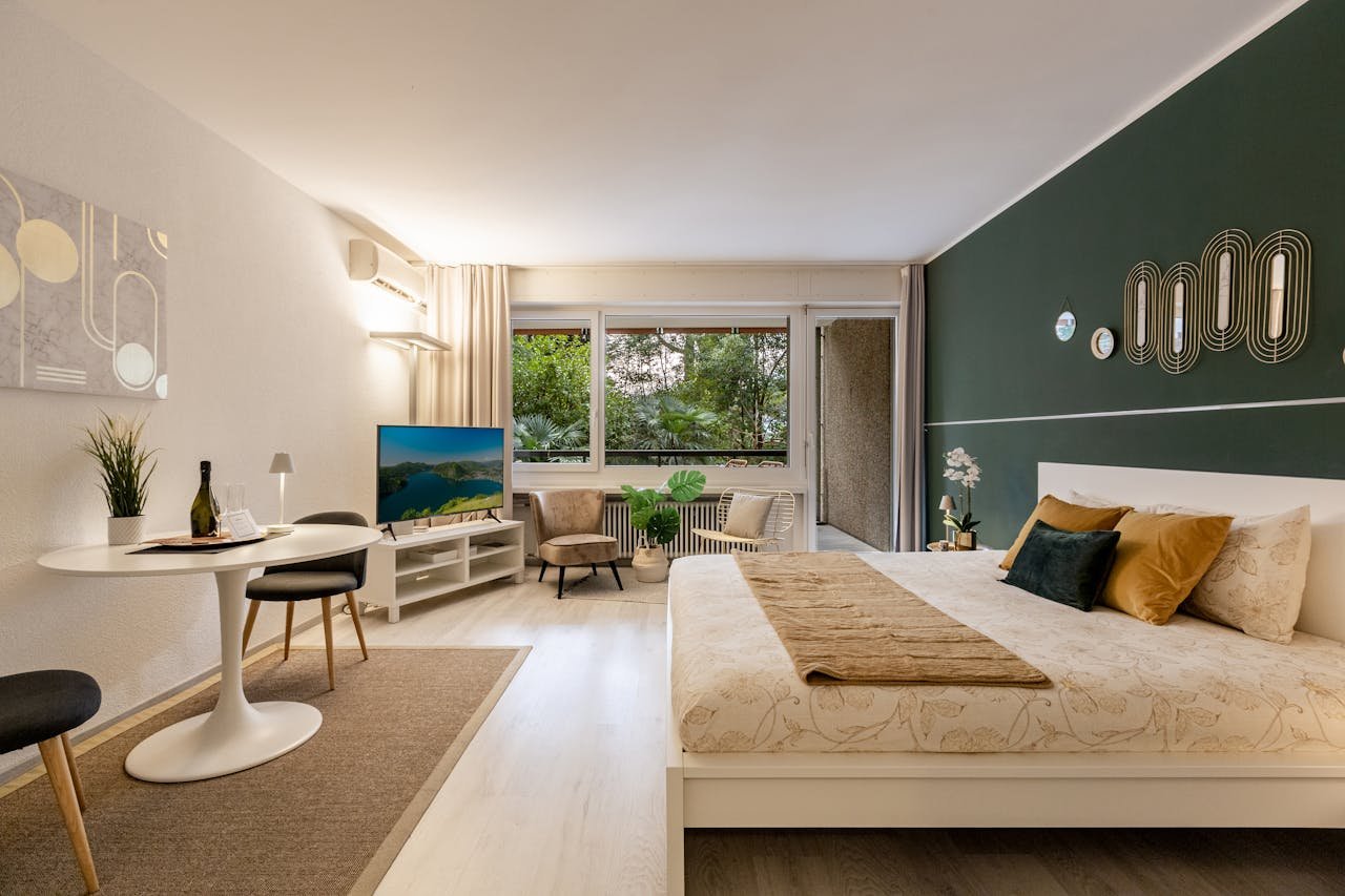 Stylish studio apartment featuring modern decor, green accent wall, and large windows.